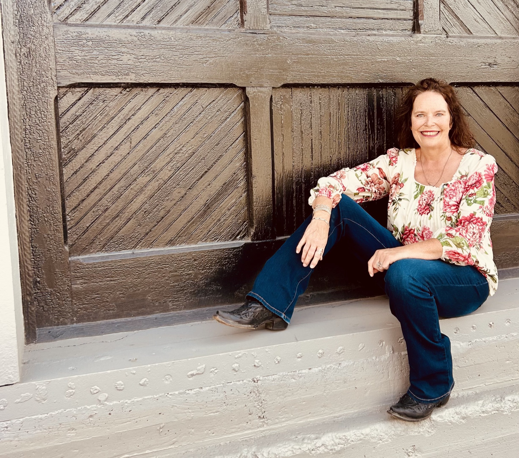 Jenny Mills sitting on the step of a wooden freight door, smiling